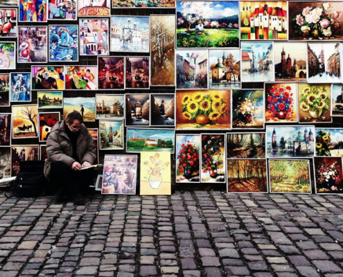 artist sitting on the street with paintings behind