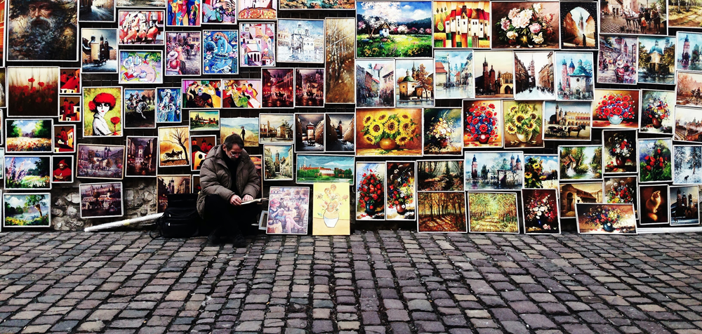 artist sitting on the street with paintings behind
