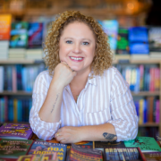 Andrea Guevara, author brand strategist leaning on stacks of books at a bookstore